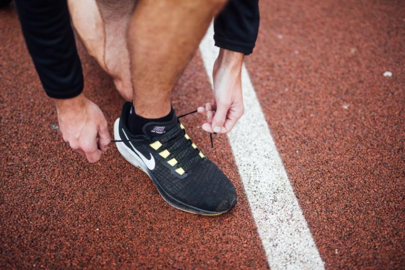 Image shows a man on a running track, tying the laces of his running shoes as he sets off for a run.